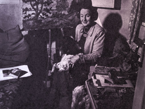 Aly holding her dog, seated in her trailer and surrounded by art supplies.